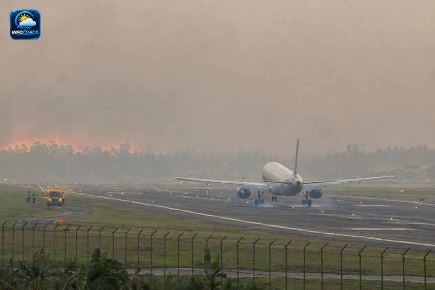 Pesawat melintas di udara dengan latar belakang langit yang diselimuti asap pekat karhutla
